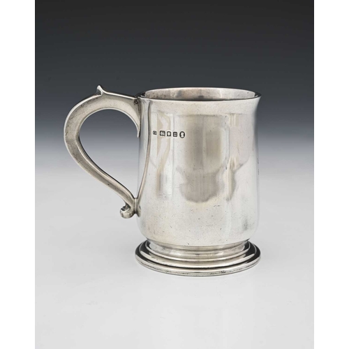 67 - A George V silver mug, with C-scroll handle, and raised thumbpiece, atop a stepped circular form foo... 