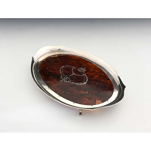 152 - A George V silver and tortoiseshell dressing table tray, of oval form with a shaped, flared rim, the... 