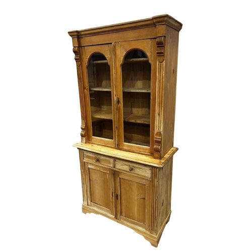 825 - A traditional stripped pine pier cabinet, the upper section with plane moulded cornice with arched g... 