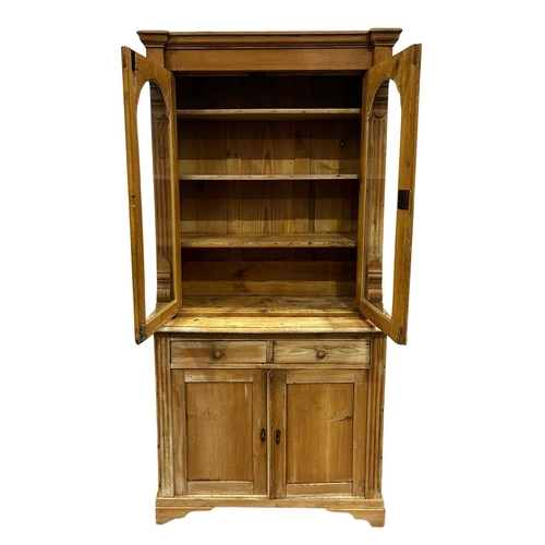 825 - A traditional stripped pine pier cabinet, the upper section with plane moulded cornice with arched g... 