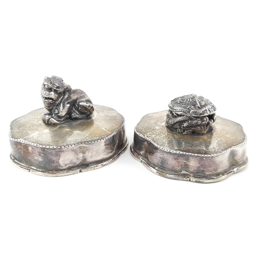 322 - Two Chinese white metal covers, serpentine borders, each with a shishi and dragon ball finial, 9cm d... 