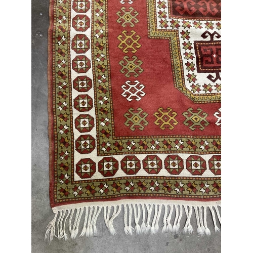 341B - Orange and green on red ground tribal rug, geometric shapes and patterns with white border and pleat... 