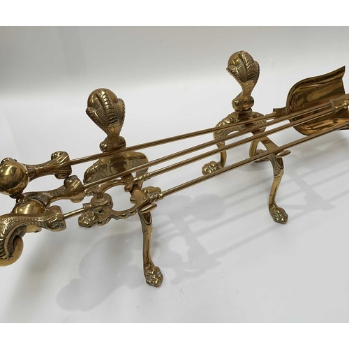 143 - A brass companion set and fire dogs, the poker, tongs and shovel all with clawed bird feet holding b... 