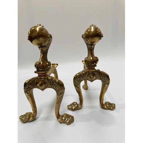 143 - A brass companion set and fire dogs, the poker, tongs and shovel all with clawed bird feet holding b... 