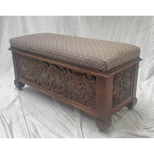 553 - An oak ottoman or blanket box, over stuffed padded top, opening to storage, heavily carved panels to... 