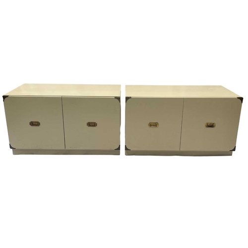 559 - A pair of campaign style two-door storage cabinets, each painted in a buttermilk colour with brassed... 