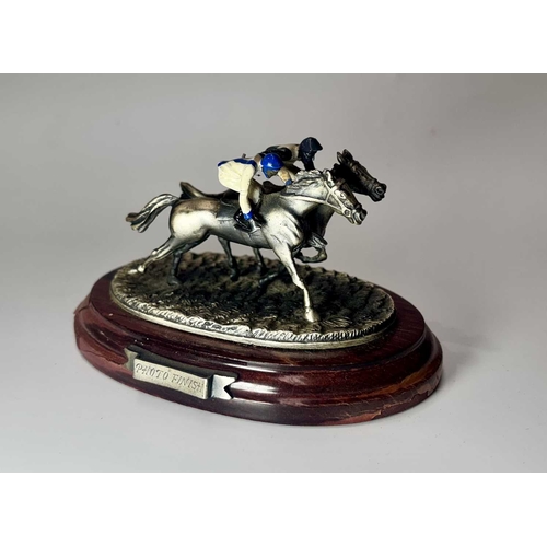 84 - A small group of hand painted, cast metal figurines of jockeys racing horses, mounted to wooden plin... 