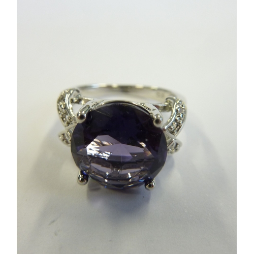 234 - An ornate silver ring centrally set with a deep amethyst-coloured hand-cut stone within pierced shou... 