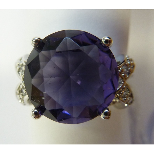 234 - An ornate silver ring centrally set with a deep amethyst-coloured hand-cut stone within pierced shou... 