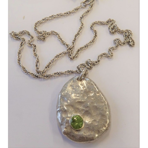 190 - A heavy modern design oval mottled silver pendant of pebble form and set with a hand-cut green gemst... 