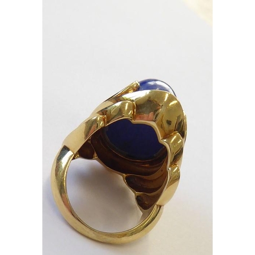 322 - A stylish 1960s lapis lazuli dress ring, the oval lapis cabochon set above a concave navette plaque ... 