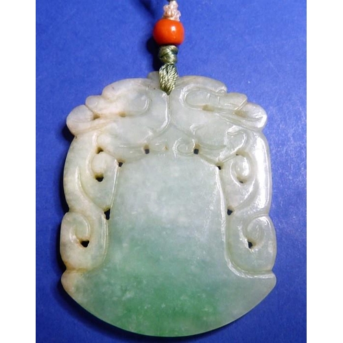 489 - A jadeite axe-form double dragon pendant on silk cord with a red-coral bead bound with seed pearls (... 