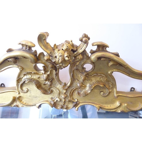 749 - A large 19th century gilt-framed wall-hanging looking glass in 18th century style; the pediment carv... 