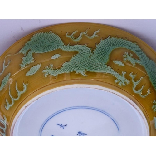 91 - A Chinese porcelain scrafitto dish; three green dragons chasing pearls amongst clouds against an oli... 