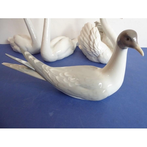 27 - Four pieces of Lladro porcelain; a matched pair of swans (approx. 22cm high), another swan furling i... 