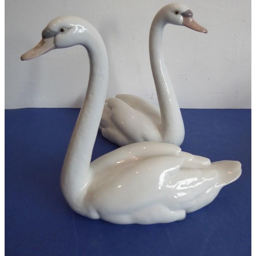 27 - Four pieces of Lladro porcelain; a matched pair of swans (approx. 22cm high), another swan furling i... 