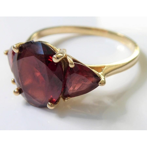 222 - A garnet ring, set with an oval mixed-cut garnet, a triangular-cut garnet to either side, the plain ... 