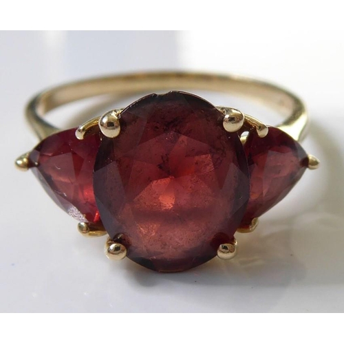 222 - A garnet ring, set with an oval mixed-cut garnet, a triangular-cut garnet to either side, the plain ... 