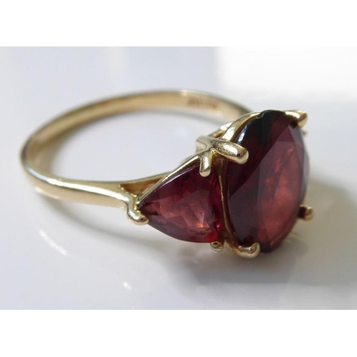 222 - A garnet ring, set with an oval mixed-cut garnet, a triangular-cut garnet to either side, the plain ... 