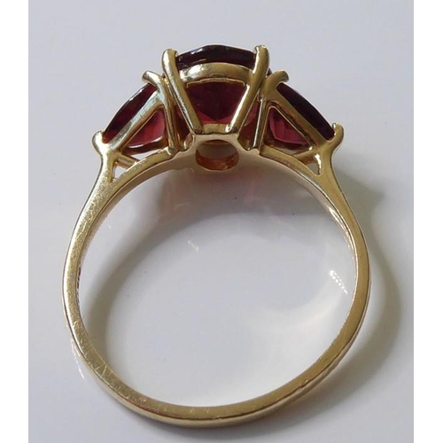 222 - A garnet ring, set with an oval mixed-cut garnet, a triangular-cut garnet to either side, the plain ... 