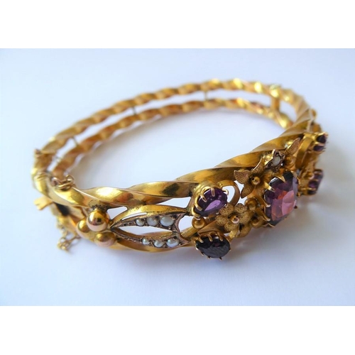 224 - An Edwardian amethyst, half pearl and 9 carat gold hinged bangle, the top section of the openwork te... 