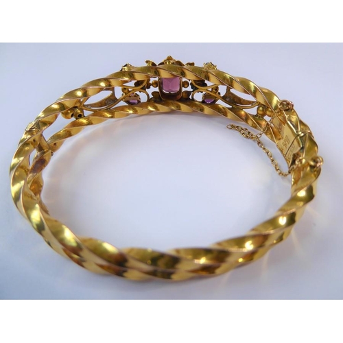 224 - An Edwardian amethyst, half pearl and 9 carat gold hinged bangle, the top section of the openwork te... 