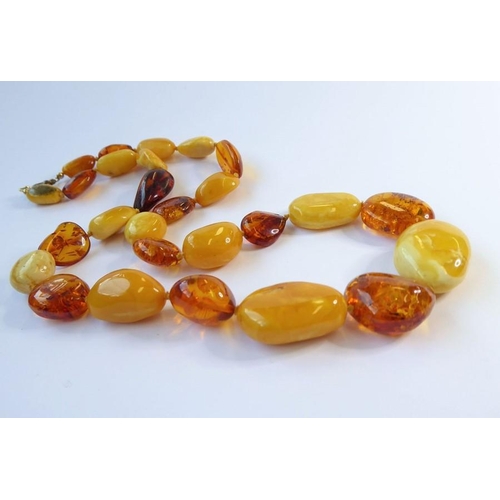 238 - Two amber bead and 'nugget' necklaces, one further and an oval amber brooch within a scrolling surro... 