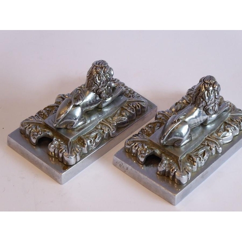 98 - A pair of heavy Art Deco period cast chrome onto brass paperweights modelled as recumbent lions on r... 