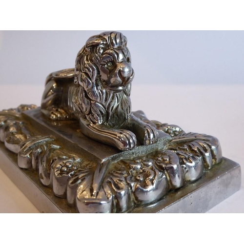 98 - A pair of heavy Art Deco period cast chrome onto brass paperweights modelled as recumbent lions on r... 