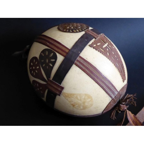 134 - An early to mid-20th century ostrich egg; decorated in relief with hand-cut leather appliques, toget... 