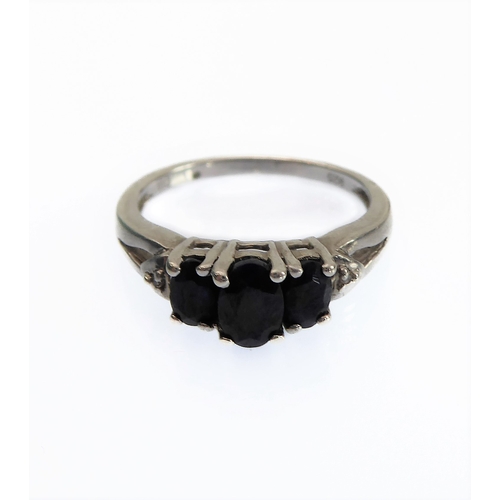 120 - A silver dress ring centrally set with three dark-blue oval stones flanked by a single small diamond... 