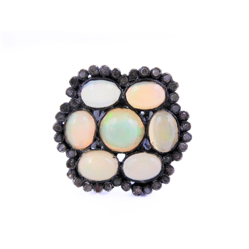 122 - An unusual black lacquered silver ring set with seven opals surrounded by small diamonds, ring size ... 