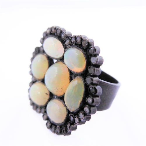 122 - An unusual black lacquered silver ring set with seven opals surrounded by small diamonds, ring size ... 