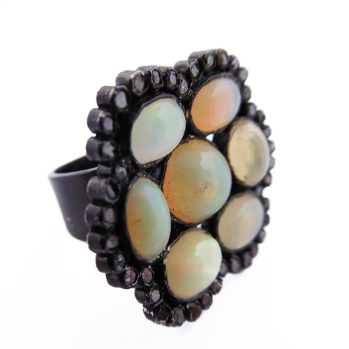 122 - An unusual black lacquered silver ring set with seven opals surrounded by small diamonds, ring size ... 