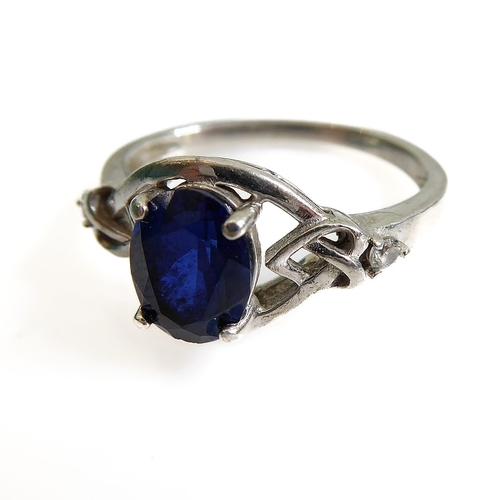 131 - A silver dress ring set with an oval vertically aligned dark-blue stone within an openwork Celtic de... 