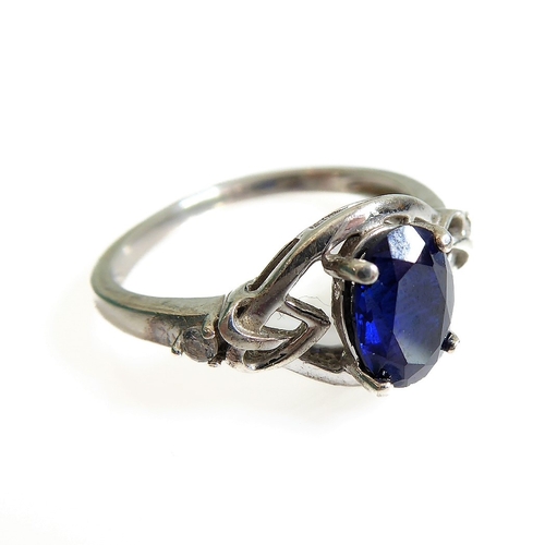 131 - A silver dress ring set with an oval vertically aligned dark-blue stone within an openwork Celtic de... 