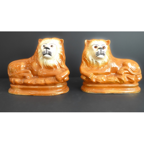 42 - A pair of 19th century Staffordshire pottery lion figures in recumbent pose and with moulded oval pl... 