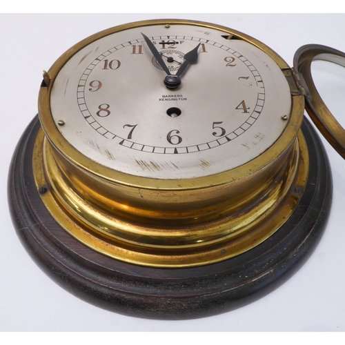 217 - A brass-cased ship's clock; the dial marked 'Barkers - Kensington' (wooden mount 28 cm in diameter)
