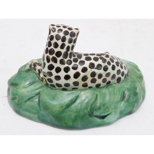 55 - A late 18th to early 19th century Pearlware model of a recumbent black spotted leopard upon an oval ... 