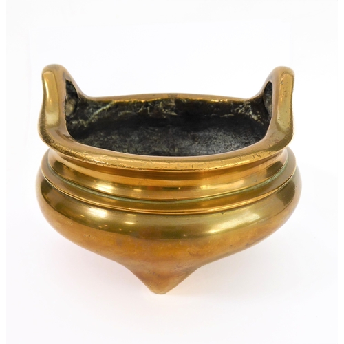 111 - A Chinese polished brass/bronze two-handled tripod censer in 17th century style: reign marks within ... 
