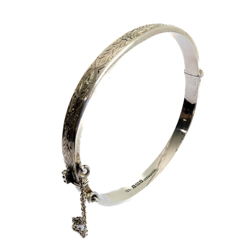 112 - A hallmarked silver bangle with hinge and safety chain: the outer edge finely foliate engraved in br... 