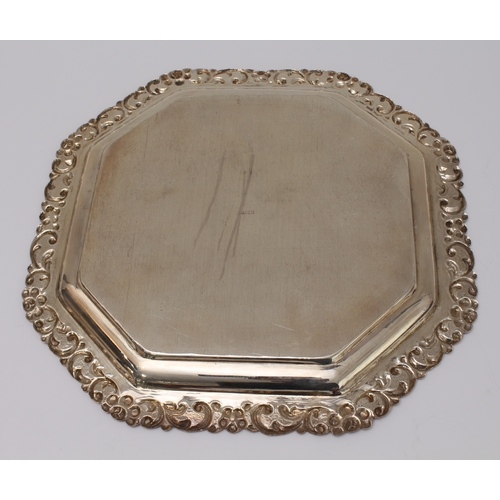 146 - An octagonal white metal presentation salver (marked 'Silver' to underside): floral style repoussé d... 