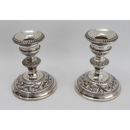 181 - A pair of modern, hallmarked silver, weighted candlesticks: spreading circular feet decorated with s... 