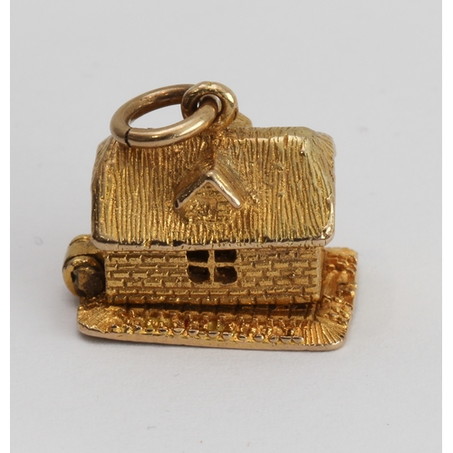 218 - A 9-carat yellow gold charm modelled as a cottage opening on a hinge to reveal a bear asleep in bed ... 