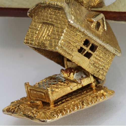 218 - A 9-carat yellow gold charm modelled as a cottage opening on a hinge to reveal a bear asleep in bed ... 