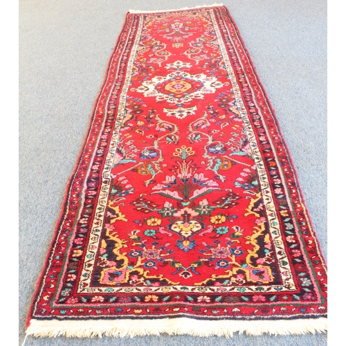 590 - A Persian Hamadan runner; red ground with ivory central medallion and sprays of flowers surrounded b... 