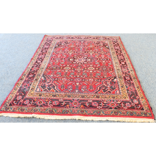 591 - A Persian Hamadan rug; red ground with blue central medallion, floral sprays surrounded by four bord... 