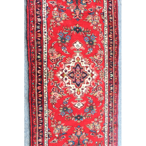 593 - A Persian Hamadan runner; red ground with ivory central medallion surrounded by flowers (294 x 89 cm... 