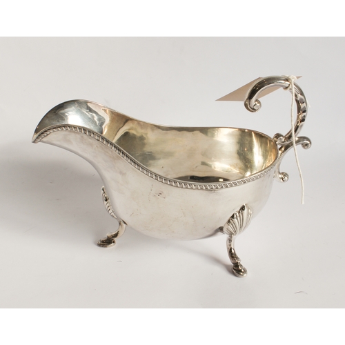 193 - A heavy hallmarked silver sauceboat; high arch scrolling handle above a gadrooned border and three s... 