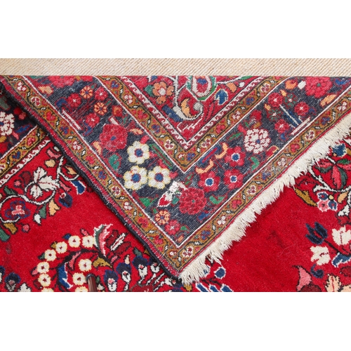 566 - A Persian rug - with a large floral medallion and spandrels on a madder ground, within a blue floral... 